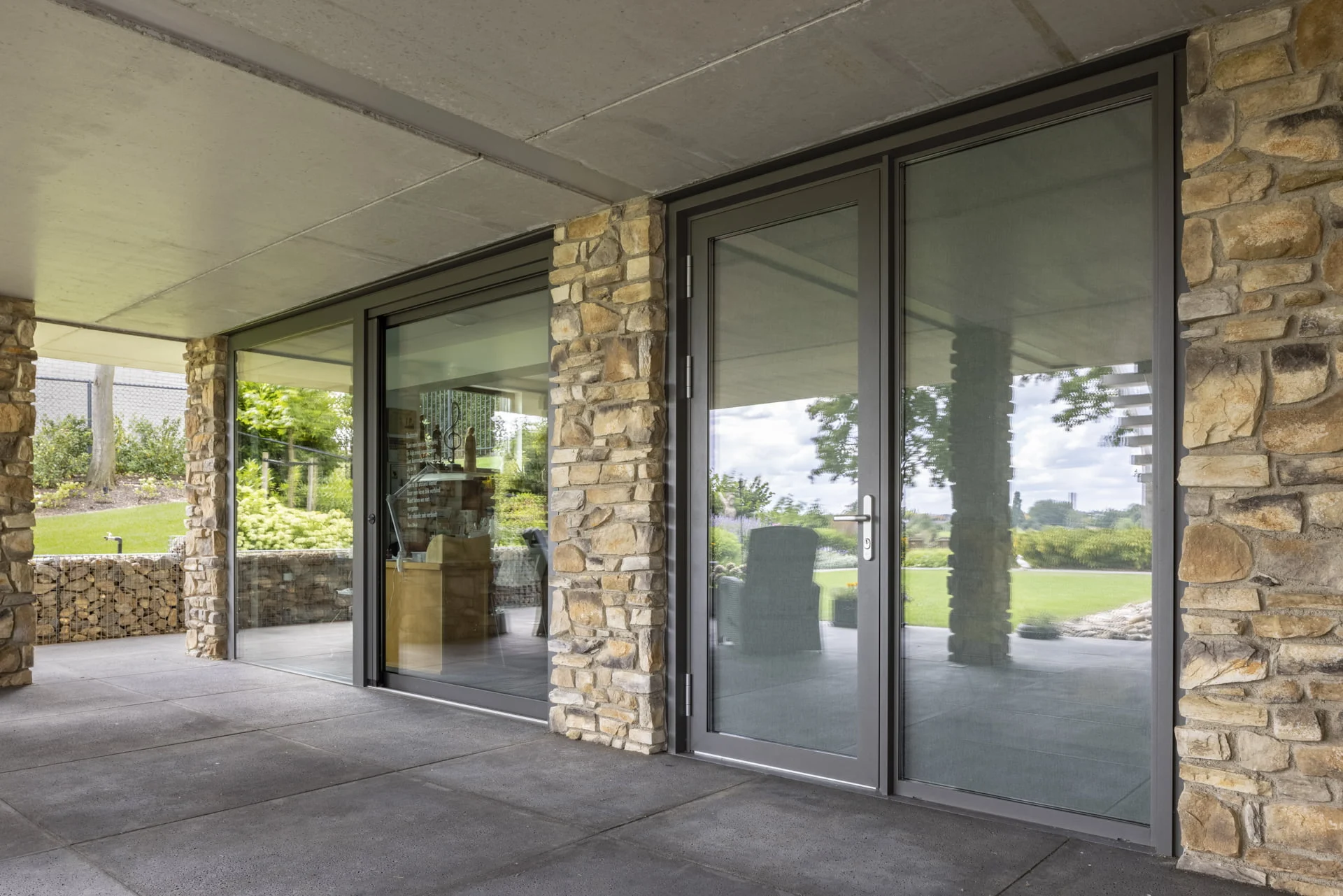 Moderne Aluprof aluminium schuifpui en achterdeur in antracietkleurig kozijn, geïntegreerd in gevel met natuursteen – Toelevering Online