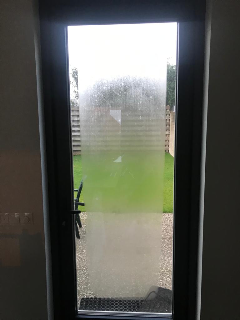 Enkele achterdeur met beslagen glas en zicht op tuin vanuit binnenzijde